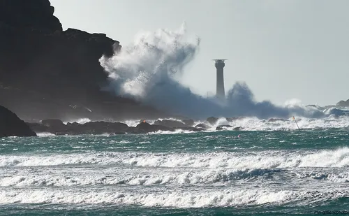 This landscape photograph captures the dramatic waves crashing against the Longships cliffs near Sennen Cove on the coast of Cornwall, United Kingdom, early in the afternoon during the winter season. The powerful sea surges and rugged cliffs are prominent, with the Longships Lighthouse standing tall as a key landmark in the background, highlighting the untamed nature of this coastal region. The turbulent ocean demonstrates the winter strength of the Atlantic, while the rocky shoreline and breaking waves showcase the natural beauty typical of Cornwall’s coastline. The lighthouse serves as a vital beacon for ships navigating these perilous waters, and the surrounding environment reflects the raw power and majesty of nature along the United Kingdom’s southwestern edge.